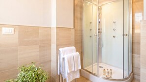 A modern bathroom with a glass-enclosed shower, beige tiles, and a potted plant.