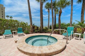 A circular hot tub surrounded by lounge chairs and palm trees, with a view of a building in the background. - Beachfront! Amazing Views! 6B Crescent Beach Club (Clearwater)