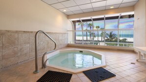 Un espace bien-être comprenant un jacuzzi, une fenêtre donnant sur les palmiers et la plage, ainsi qu'un sol carrelé.