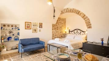 Una stanza accogliente con un letto, un divano blu, un tavolino in vetro con piatti e un muro in pietra.