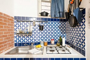 Una cocina con un lavamanos, estufa y utensilios colgando.