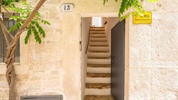 Ein Steinhaus mit einer Treppe, die zu einer dunklen Tür führt, einem Schild mit der Nummer 13 und einem gelben Schild, das einen Bereich mit Videoüberwachung kennzeichnet.