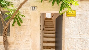 A stone building with a staircase leading to a dark door, a number '13' sign, and a yellow sign indicating a video surveillance area. - Corte Fiorita – Intimate Suite in the historic center (Bitonto)