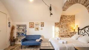 A room with a stone wall, a bed with white bedding, a blue sofa, a small table, and a hanging light fixture.
