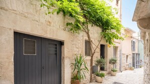 Un estrecho callejón empedrado con una puerta de madera oscura, plantas en macetas y un edificio de fachada de piedra.