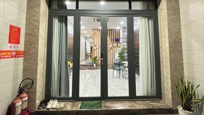 Entrada de hotel con puerta de cristal, extintor y planta en maceta.