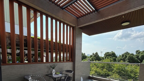 Un patio moderno al aire libre con techo de madera, dos sillas de mimbre blanco y negro, una mesita y una planta en maceta.