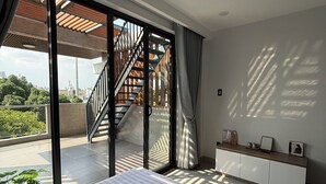 Un dormitorio con cama, mesita de noche, ventana con cortinas, escalera que lleva a un espacio exterior y vista a zonas verdes.