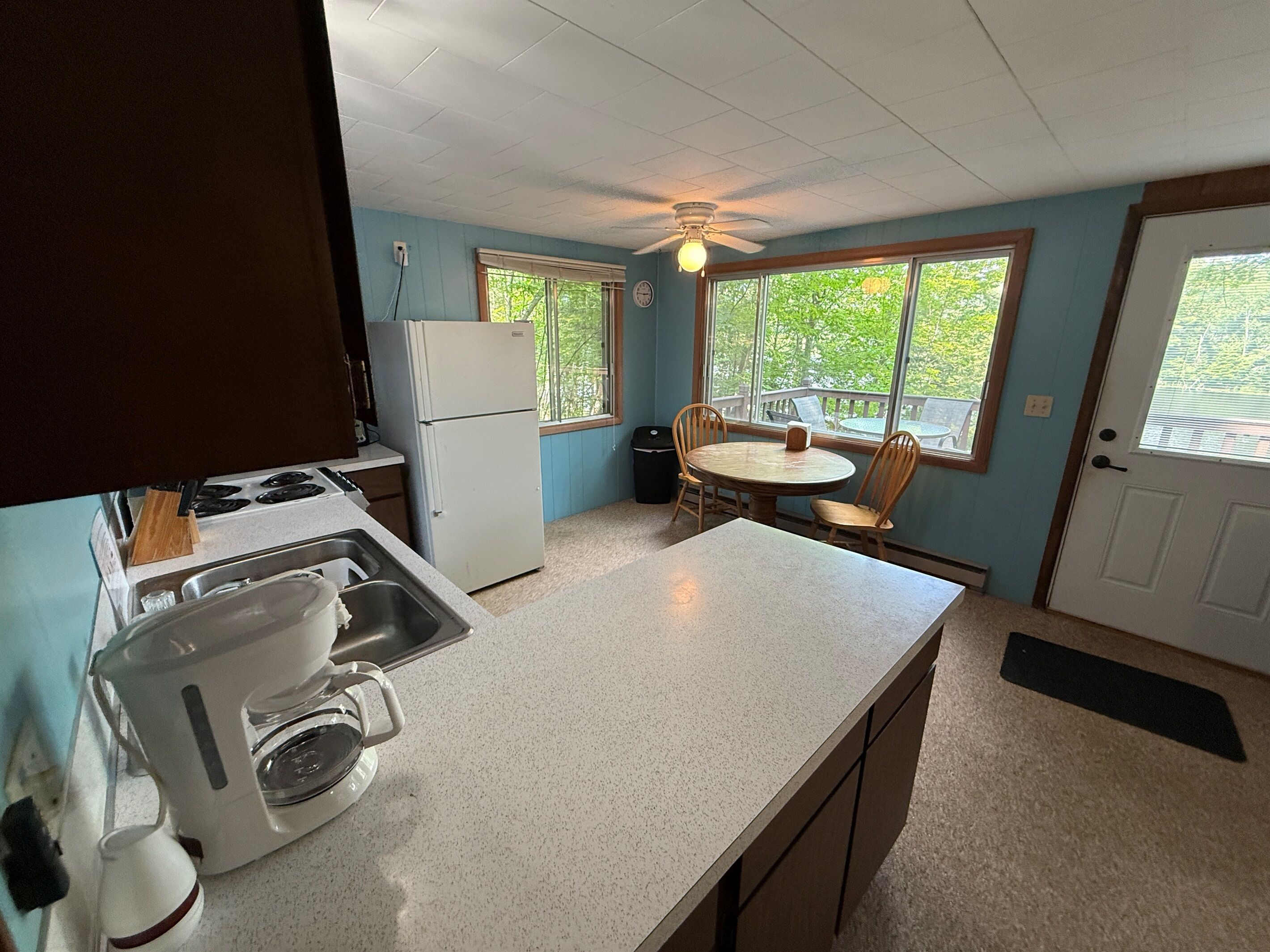 Cocina compacta con refrigerador, estufa y cafetera. Hay una mesa de comedor con sillas y una ventana con vistas a la vegetación.