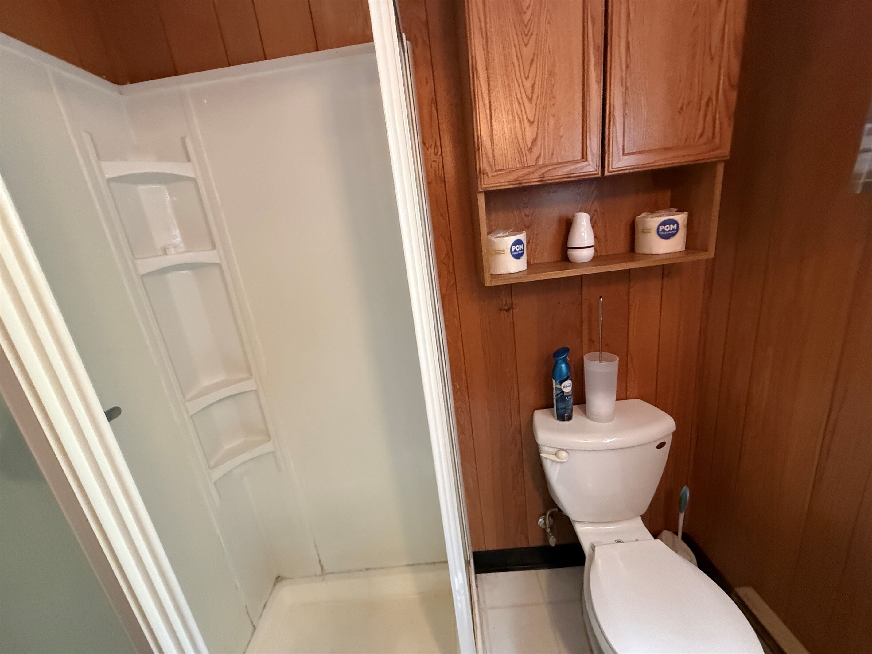 A bathroom with a white toilet, wooden cabinets, and a shelf with toiletries.