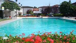 A swimming pool surrounded by colorful flowers and white buildings with red-tiled roofs.