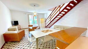 A compact living space with a dining area, a sofa, a TV, and a staircase.