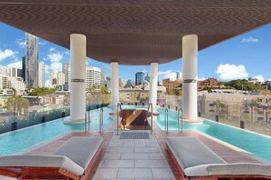 An infinity pool with lounge chairs, a view of the city skyline, and a covered area with columns. - The Valley Pad | 2BR with Style (Brisbane)