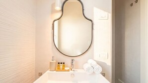 A modern bathroom with a freestanding bathtub, a round mirror, and toiletries on the side. - Dimora Anna - Beachfront Apartment (Bari)