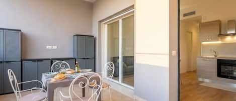 A modern apartment with a dining area, kitchen, and sliding glass doors leading to a balcony.