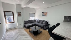 A modern living room with a sectional sofa, a coffee table, and a dining area with chairs. - Modern 2-Bedroom Apartment  in the Heart of Shoreditch (London)