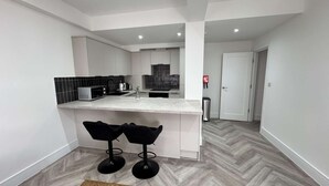 A modern kitchen with a white countertop, black bar stools, and a herringbone-patterned floor. - Modern 2-Bedroom Apartment  in the Heart of Shoreditch (London)