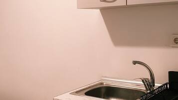 A small kitchenette with a sink, cabinets, and a bed.