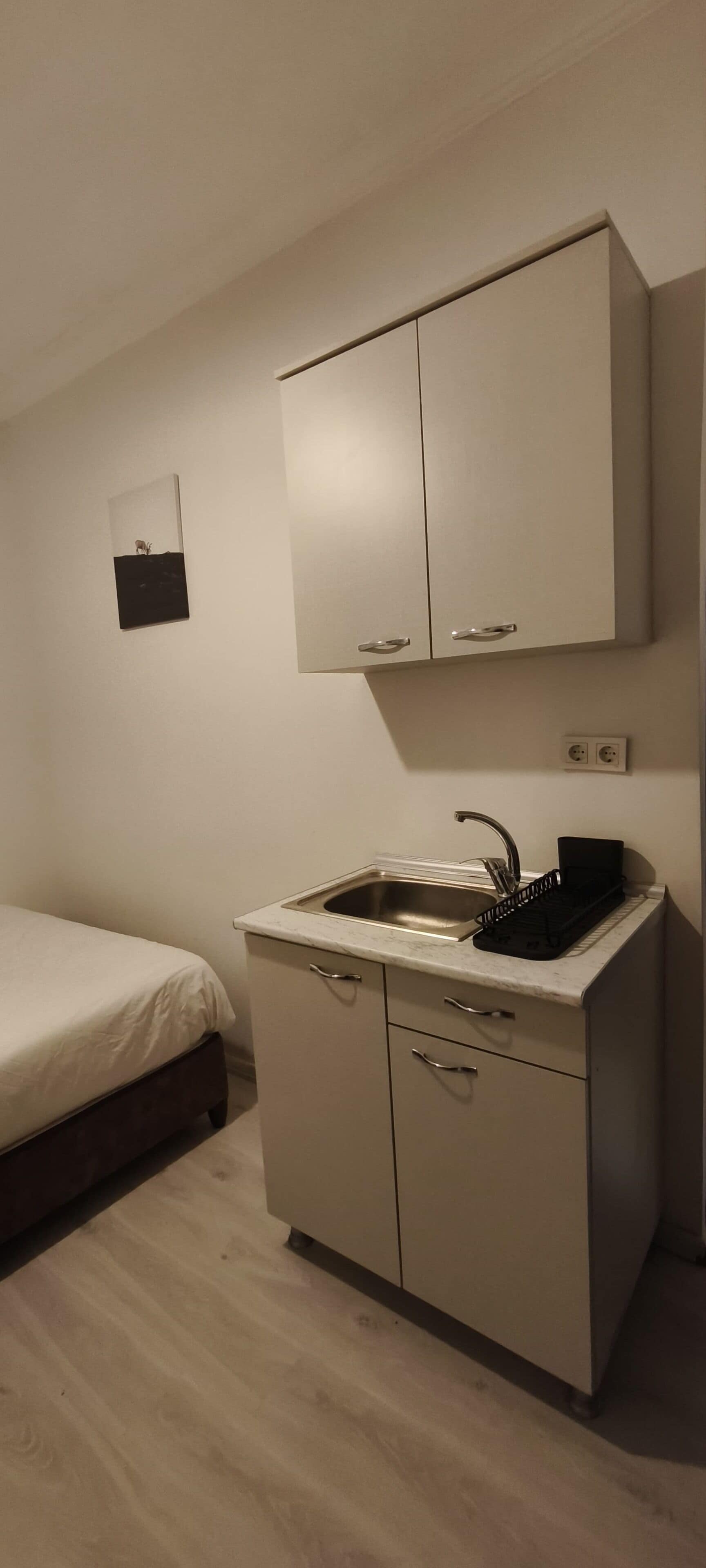 A small kitchenette with a sink, cabinets, and a bed.