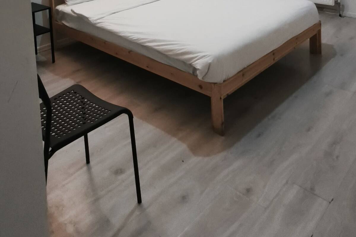 A bedroom with a wooden bed, a chair, a desk, and a radiator.