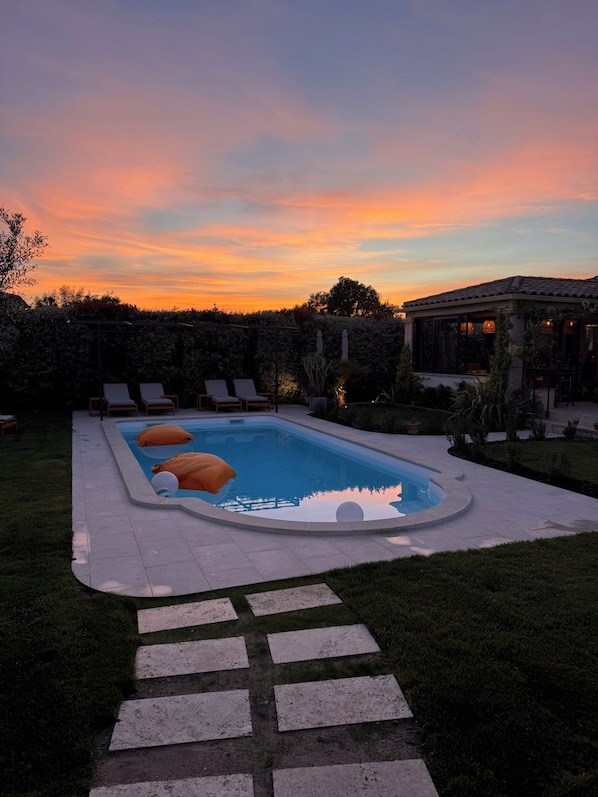 A rectangular swimming pool with a paved deck, surrounded by a grassy area and a hedge.