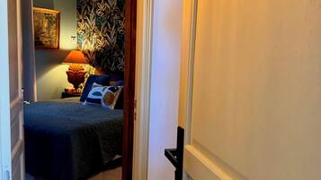 Een hotelkamer met een bed, nachtkastje, lamp en een muur met een bladmotief.
