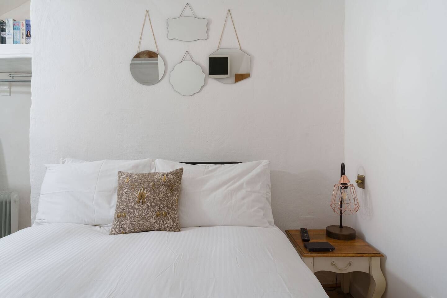 A neatly made bed with white linens and a patterned pillow, a bedside table with a lamp, and wall-mounted mirrors.