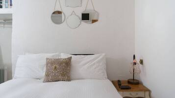 A neatly made bed with white linens and a patterned pillow, a bedside table with a lamp, and wall-mounted mirrors.