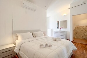 A bedroom with a bed, a bedside table, a dresser, a mirror, and a stone wall.