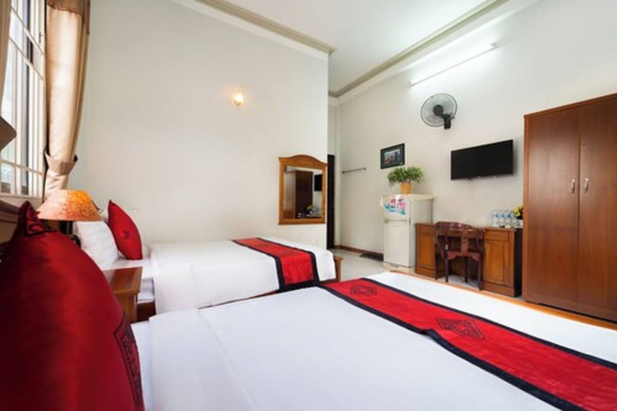 Una camera d'albergo con due letti, una scrivania, un armadio, una televisione e una finestra con tende.
