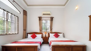 A hotel room with two wooden beds, a window with bars, an air conditioning unit, and a nightstand with a lamp. - Belvilla Comfort Stays Near Bui Vien Wal (Ho Chi Minh City)