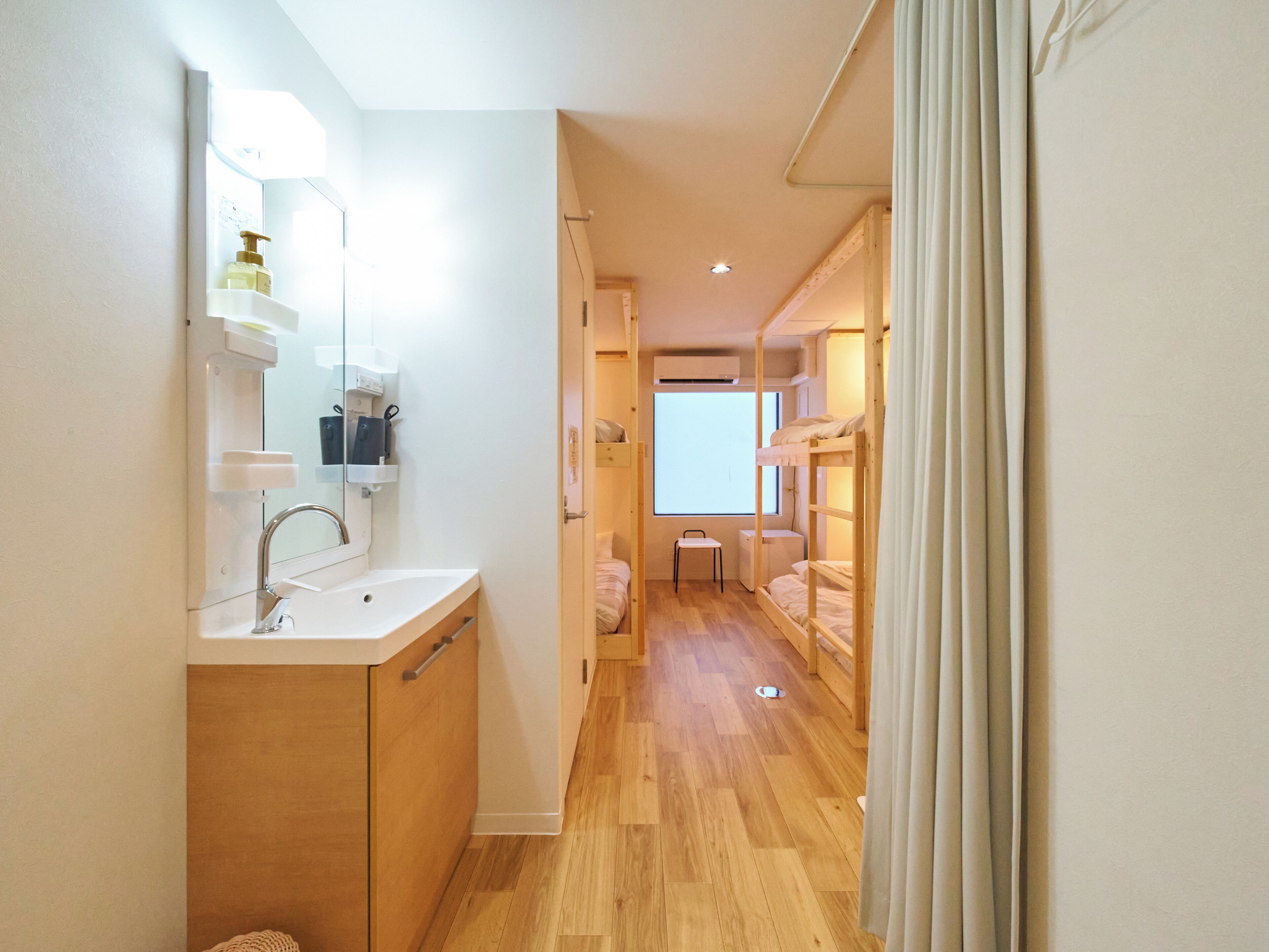 A narrow hallway with a wooden floor, a white sink, and a mirror. A bunk bed is visible in the background.