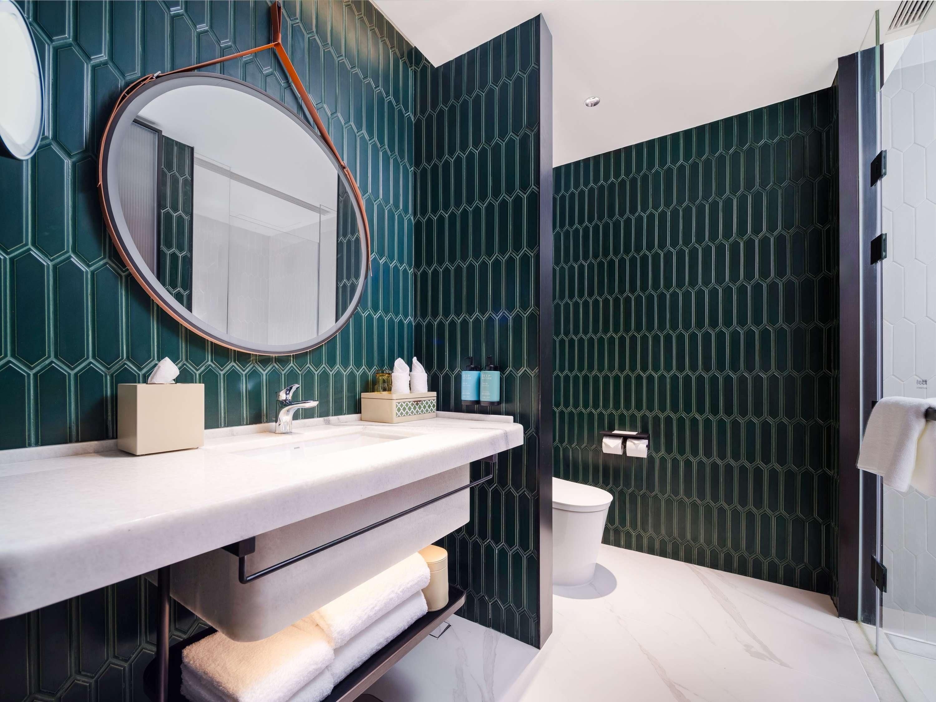 Une salle de bain moderne avec un grand miroir rond, un lavabo et des toilettes.