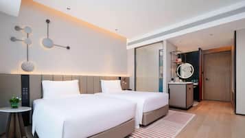 A modern hotel room with two beds, a small table with a plant, a mirror, and a bathroom with a shower.