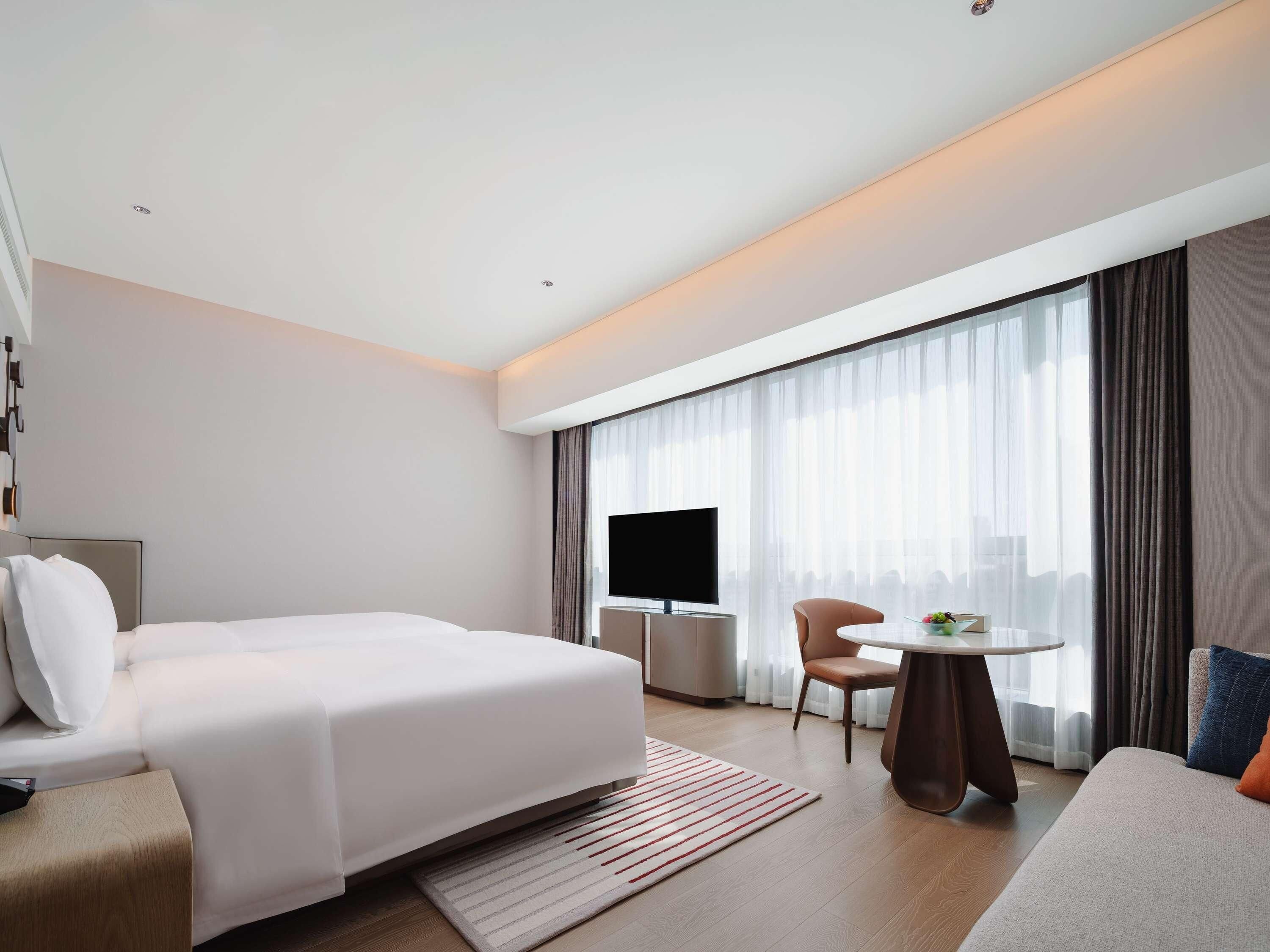 Ein modernes Hotelzimmer mit einem großen Bett, einem Fernseher, einem kleinen Tisch und einer Couch.