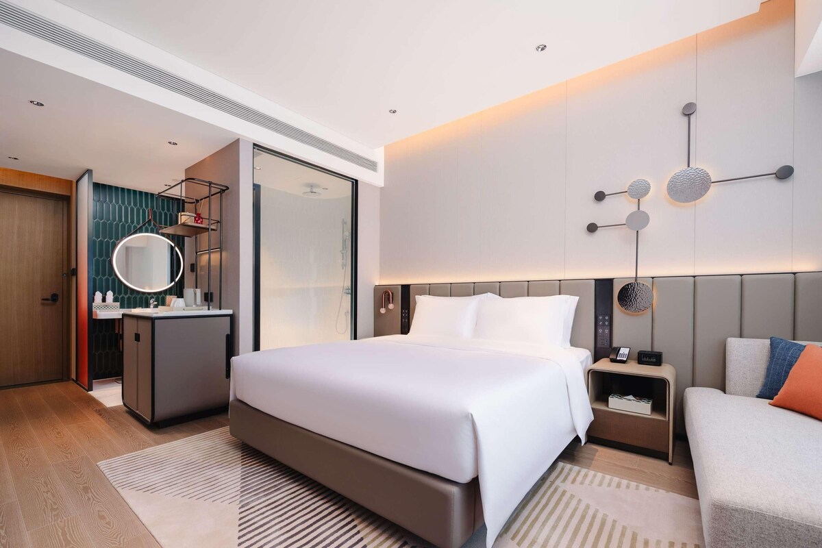 Une chambre d’hôtel moderne équipée d’un grand lit, d’un bureau, d’une coiffeuse avec miroir et d’une douche.