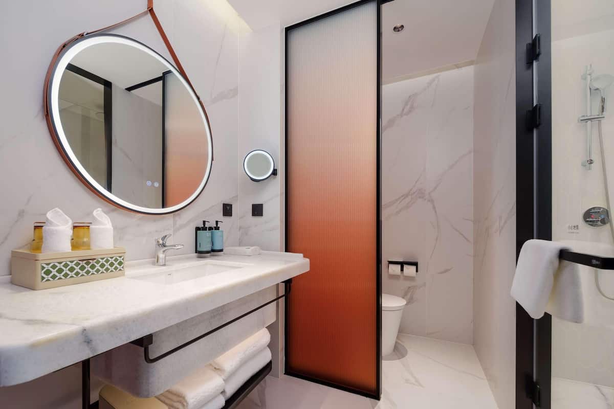 Un baño moderno con lavamanos de mármol, un espejo redondo, un perchero y una zona de ducha.