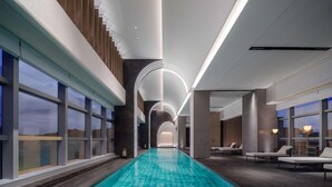 A modern indoor swimming pool with a clear view of the sky through large windows, a long poolside area with lounge chairs, and a contemporary design with clean lines and minimalistic decor. - Novotel Xiamen Downtown (Xiamen)