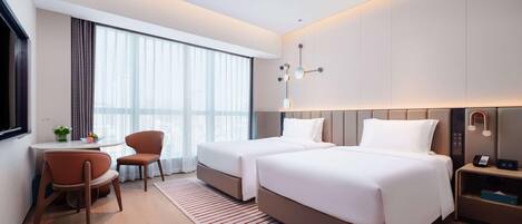 A modern hotel room with two beds, a desk, a chair, and a large window with curtains.