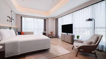 A modern hotel room with a large bed, a TV, a desk, and a chair.