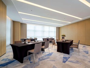 Ein moderner Konferenzraum mit mehreren Tischen und Stühlen, großen Fenstern mit durchscheinenden Vorhängen und einem gemusterten Teppich.