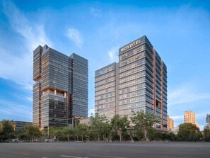 Two Novotel hotel buildings with a modern glass facade, located in an urban setting with trees in the foreground.