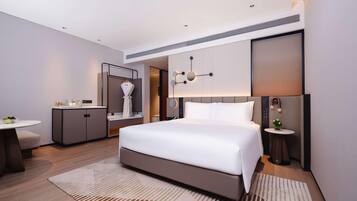A modern hotel room with a large bed, a desk, a vanity, and a small table with a plant.