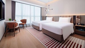 A modern hotel room with two beds, a desk, a chair, and a large window with curtains. - Novotel Xiamen Downtown (Xiamen)