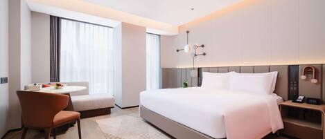 Una habitación de hotel moderna con una cama grande, un escritorio con una silla, una mesita con un frutero y una mesita de noche con un reloj.