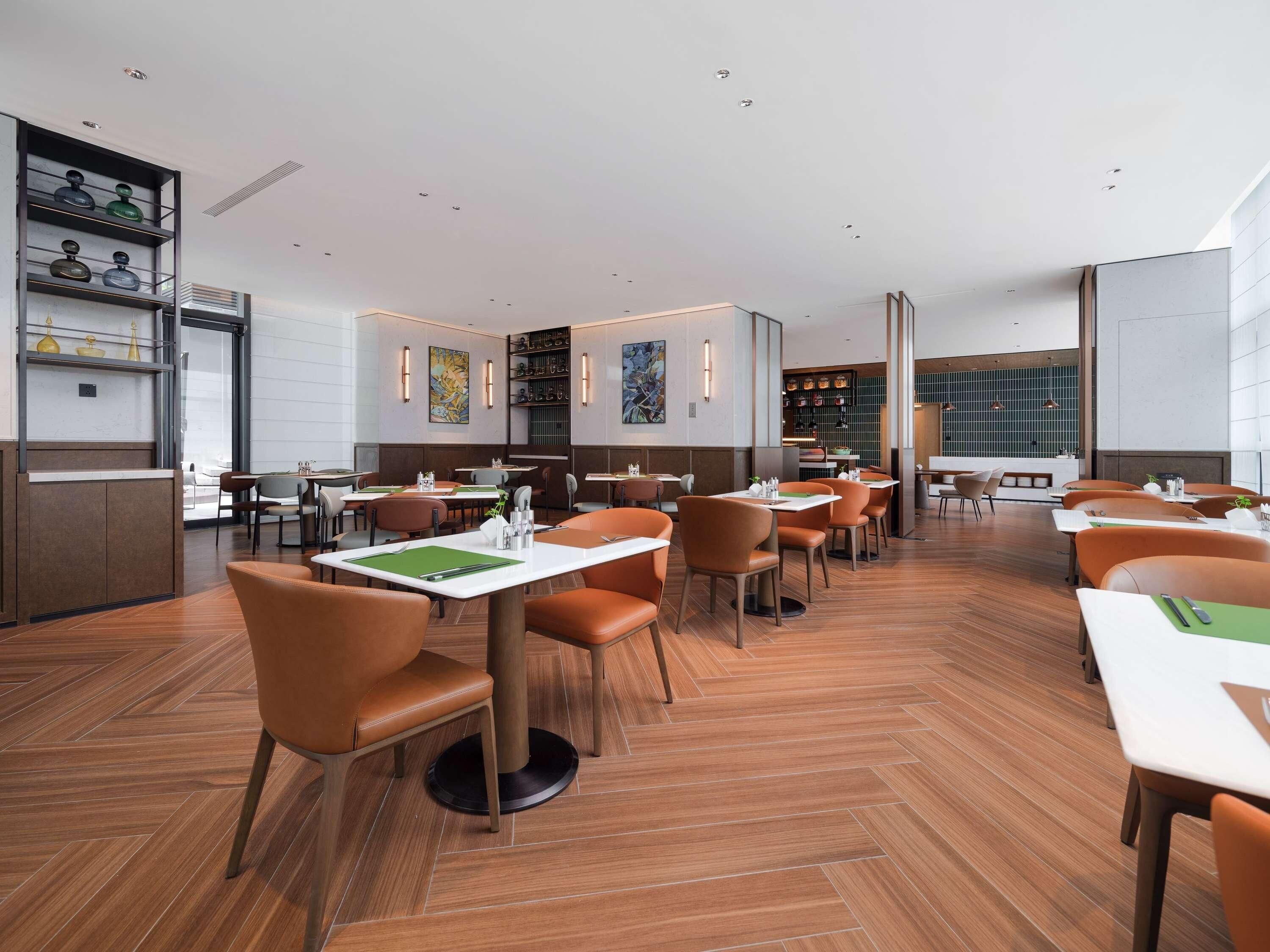 Ein modernes Restaurant mit Holzböden, orangefarbenen Stühlen und weißen Tischen.