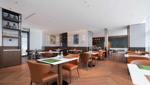 A modern restaurant with wooden floors, orange chairs, and white tables. - Novotel Xiamen Downtown (Xiamen)