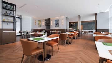 Ein modernes Restaurant mit Holzböden, orangefarbenen Stühlen und weißen Tischen.