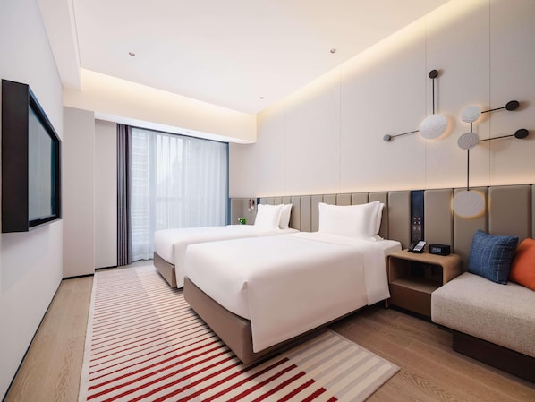 Een moderne hotelkamer met twee bedden, een groot raam, een flatscreen televisie en een nachtkastje met telefoon en wekker.