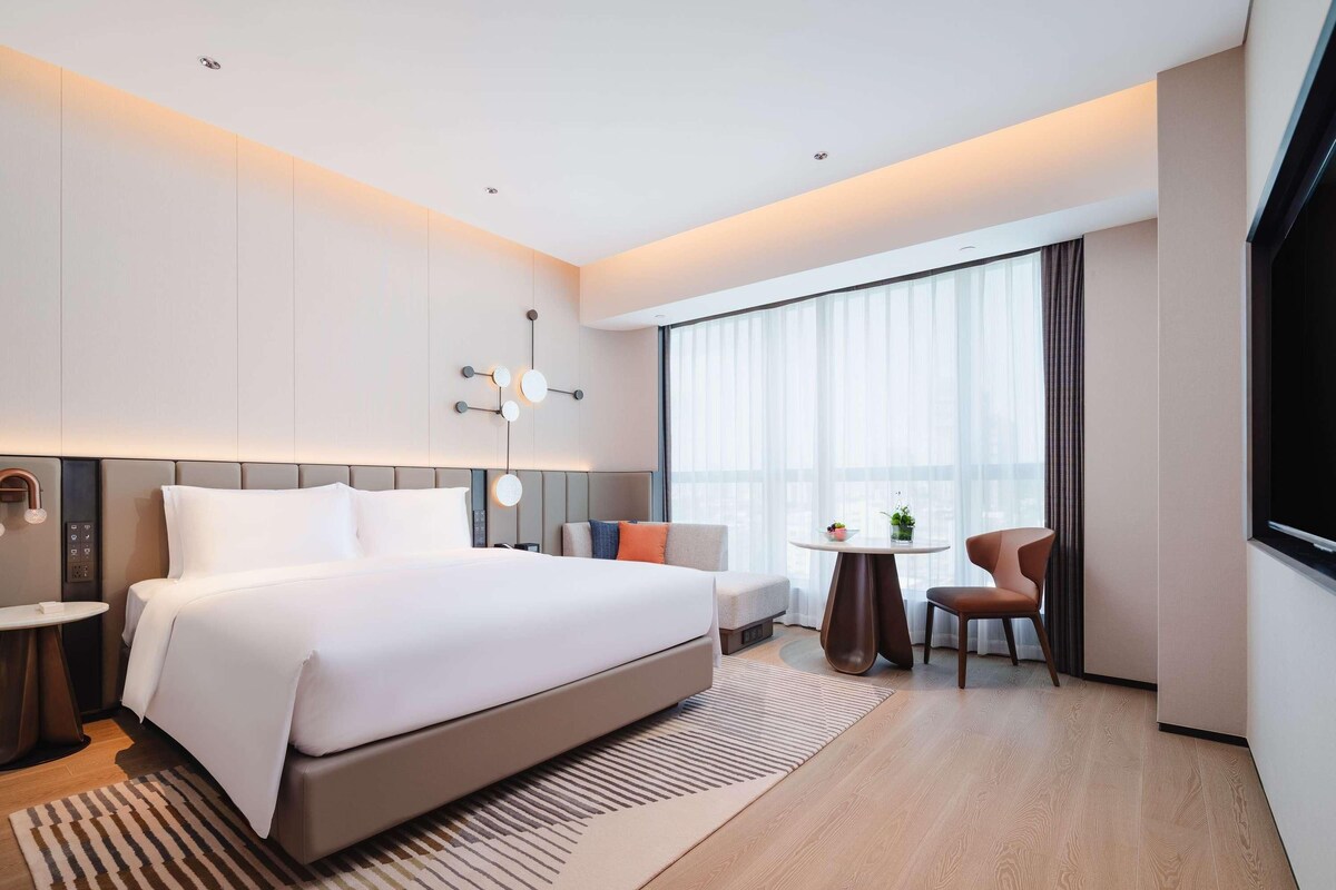 Ein modernes Hotelzimmer mit einem großen Bett, einem kleinen runden Tisch, einer Couch und einem Fernseher.
